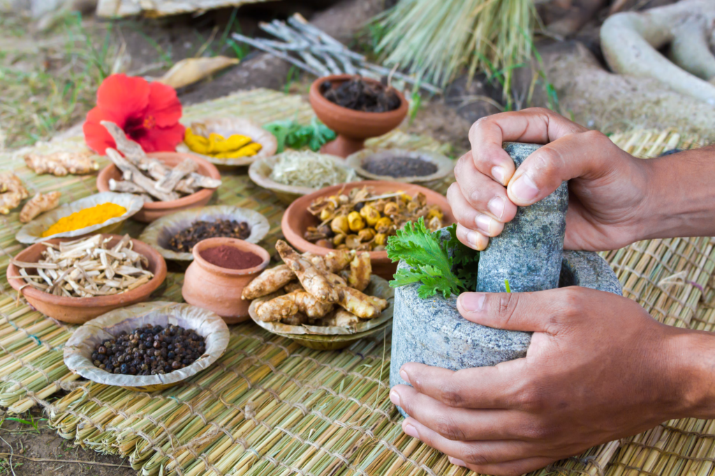 Hands grinding herbs with a mortar and pestle surrounded by spices, showcasing ayurvedic practices and benefits of ayurveda in traditional medicine