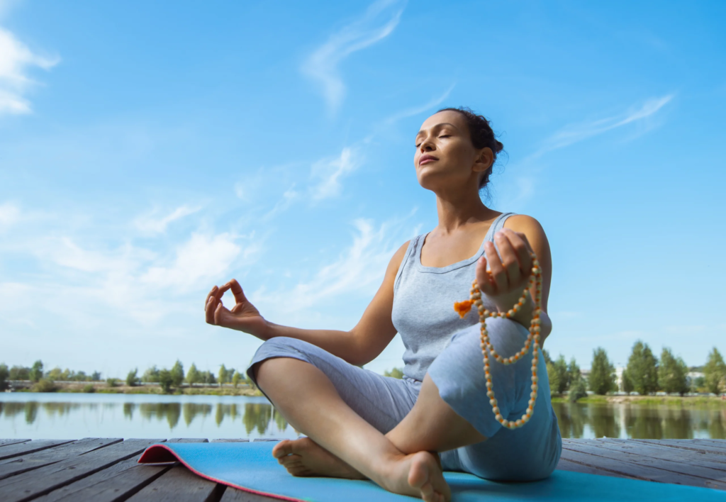 Person practicing meditation for emotional well-being on a yoga mat by a lake, showcasing the benefits of meditation in a serene outdoor setting